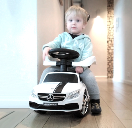 Dwuletni chłopiec jeździ po domu autkiem marki Mercedes. Jeździk posiada personalizację na masce z imieniem Kuba.