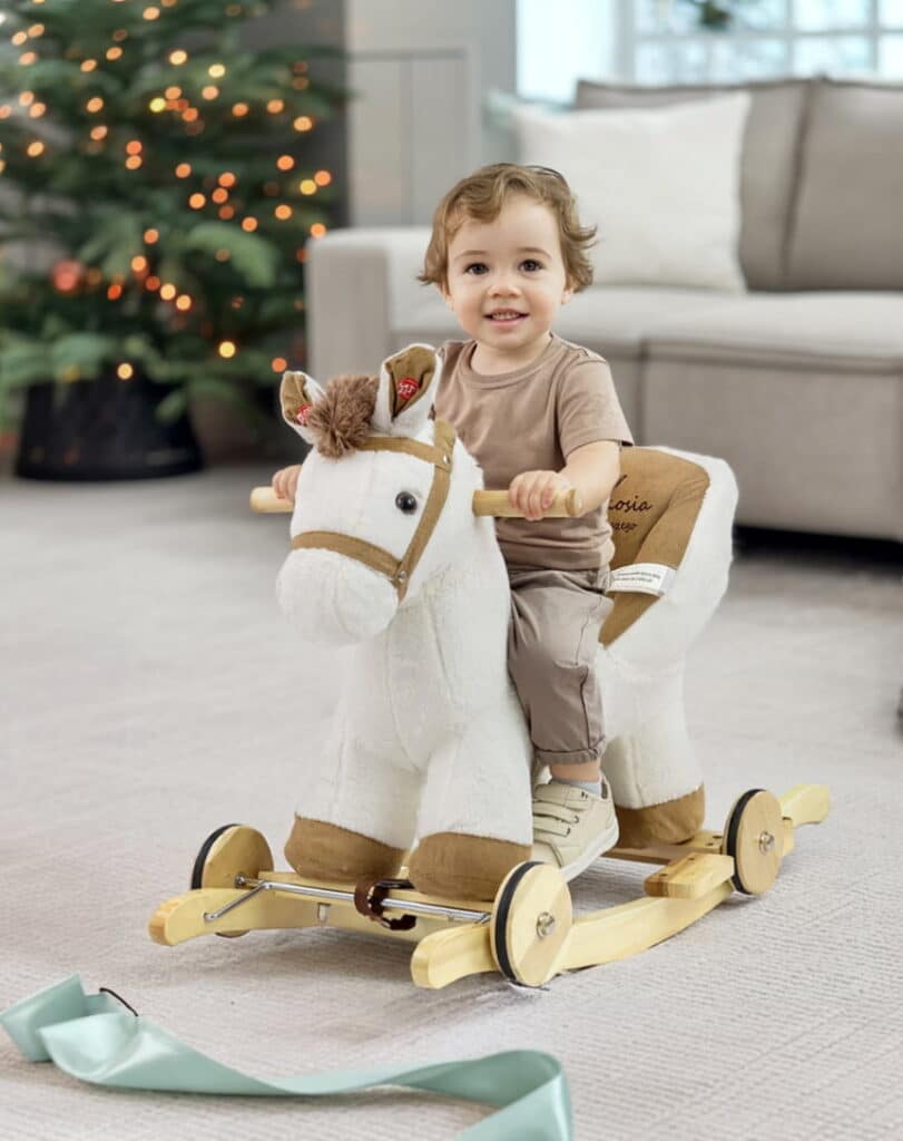 Einjähriger Junge sitzt auf einem Schaukelpferd. Weihnachtsgeschenk.